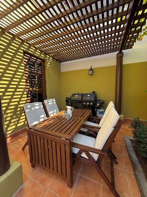 A patio with a wooden table and chairs, a grill, and a pergola structure. - Villa Amore (Nopolo)