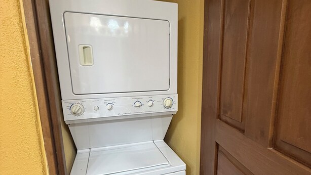 A compact laundry room with a washer and dryer, a wooden door, and a vent on the wall. - Villa Amore (Nopolo)