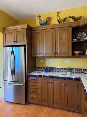 A kitchen with wooden cabinets, a stainless steel refrigerator, and decorative wall art. - Villa Amore (Nopolo)