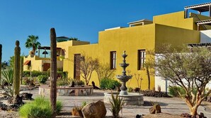 A desert-style building with a yellow facade, a fountain, and cacti in the courtyard. - Villa Amore (Nopolo)