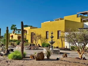 A desert-style building with a yellow facade, a fountain, and cacti in the courtyard. - Villa Amore (Nopolo)