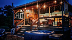 Una cabaña rústica con un porche cubierto, un jacuzzi y un comedor con mesas al aire libre.