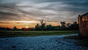 Un chemin de gravier mène à une structure en bois, avec un coucher de soleil en arrière-plan.
