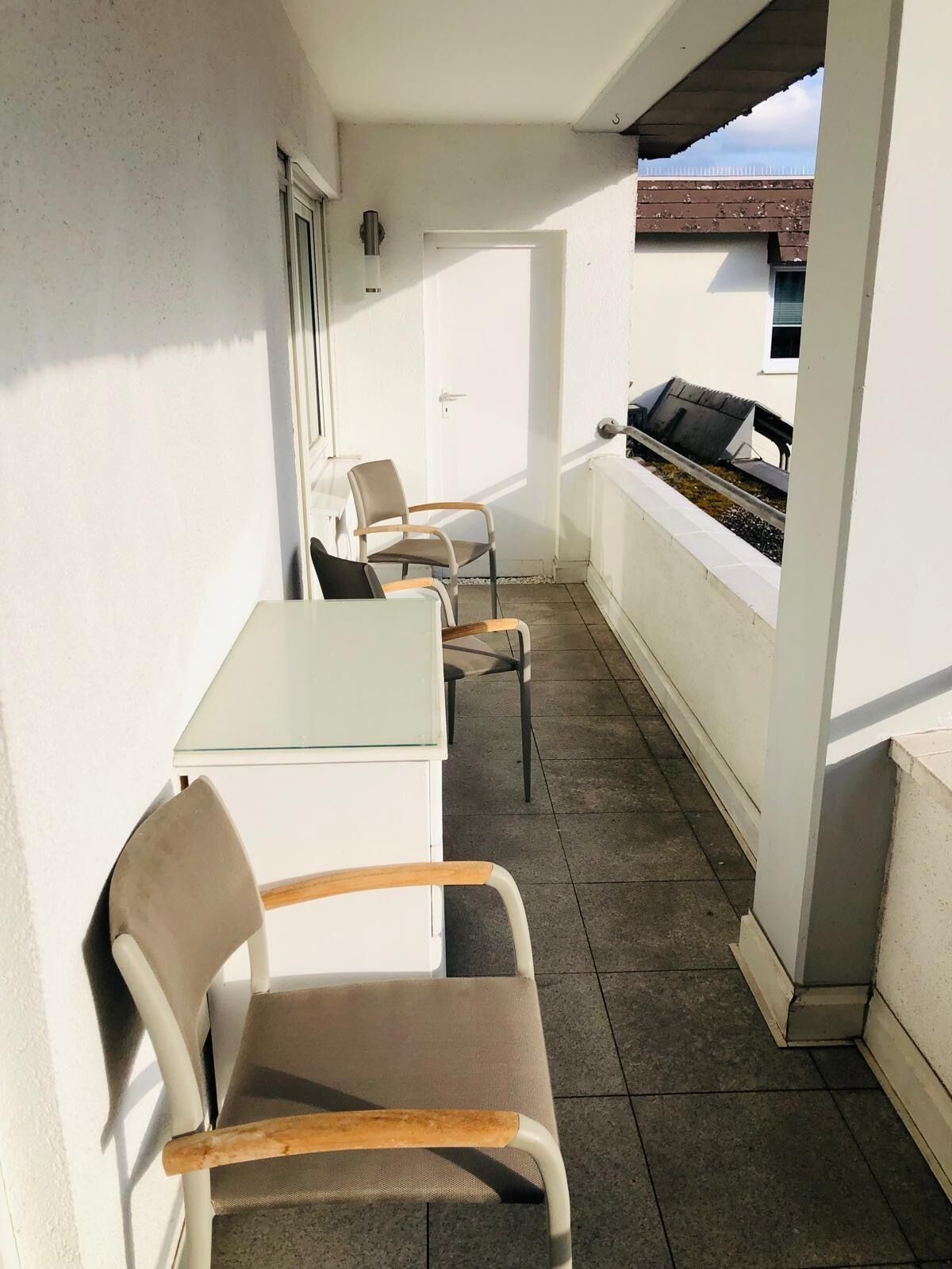 A balcony with a table and chairs, a grill, and a door.