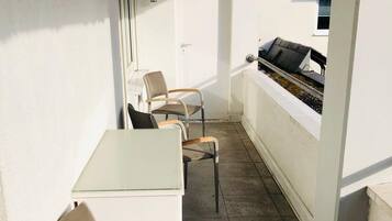 A balcony with a table and chairs, a grill, and a door.