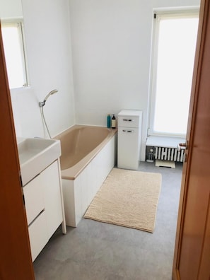 Ein Badezimmer mit einer Badewanne, einer Dusche, einem kleinen Schrank und einem Heizkörper.