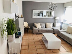 Ein modernes Wohnzimmer mit einem grauen Sofa, einem weißen Couchtisch und einer Topfpflanze.