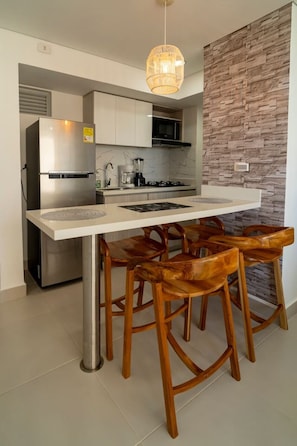 A modern kitchen with a central island, bar stools, stainless steel appliances, and a stone-textured accent wall. - Golden Breeze Apartment • Beach • Seaview • Pool (Cartagena)
