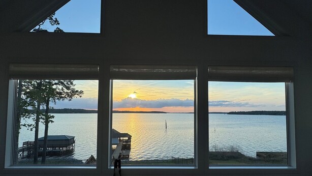 Une pièce dotée d’une grande fenêtre donnant sur un lac, un quai et un coucher de soleil.