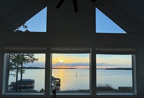 Une pièce dotée d’une grande fenêtre donnant sur un lac, un quai et un coucher de soleil.