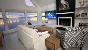 Un salon moderne doté d’une grande fenêtre, d’un téléviseur à écran plat, d’une cheminée et d’un fauteuil à motifs.