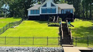 Une maison moderne dotée d’une grande terrasse, d’un escalier menant à un deuxième étage et offrant une vue sur une étendue d’eau.