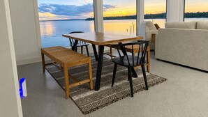 Un intérieur moderne comprenant un coin repas, un canapé et de grandes fenêtres donnant sur un lac et offrant une vue sur le coucher de soleil.