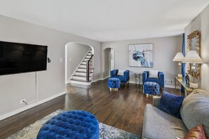 Ein modernes Wohnzimmer mit Flachbildfernseher, einer Treppe und blauen Polstermöbeln.