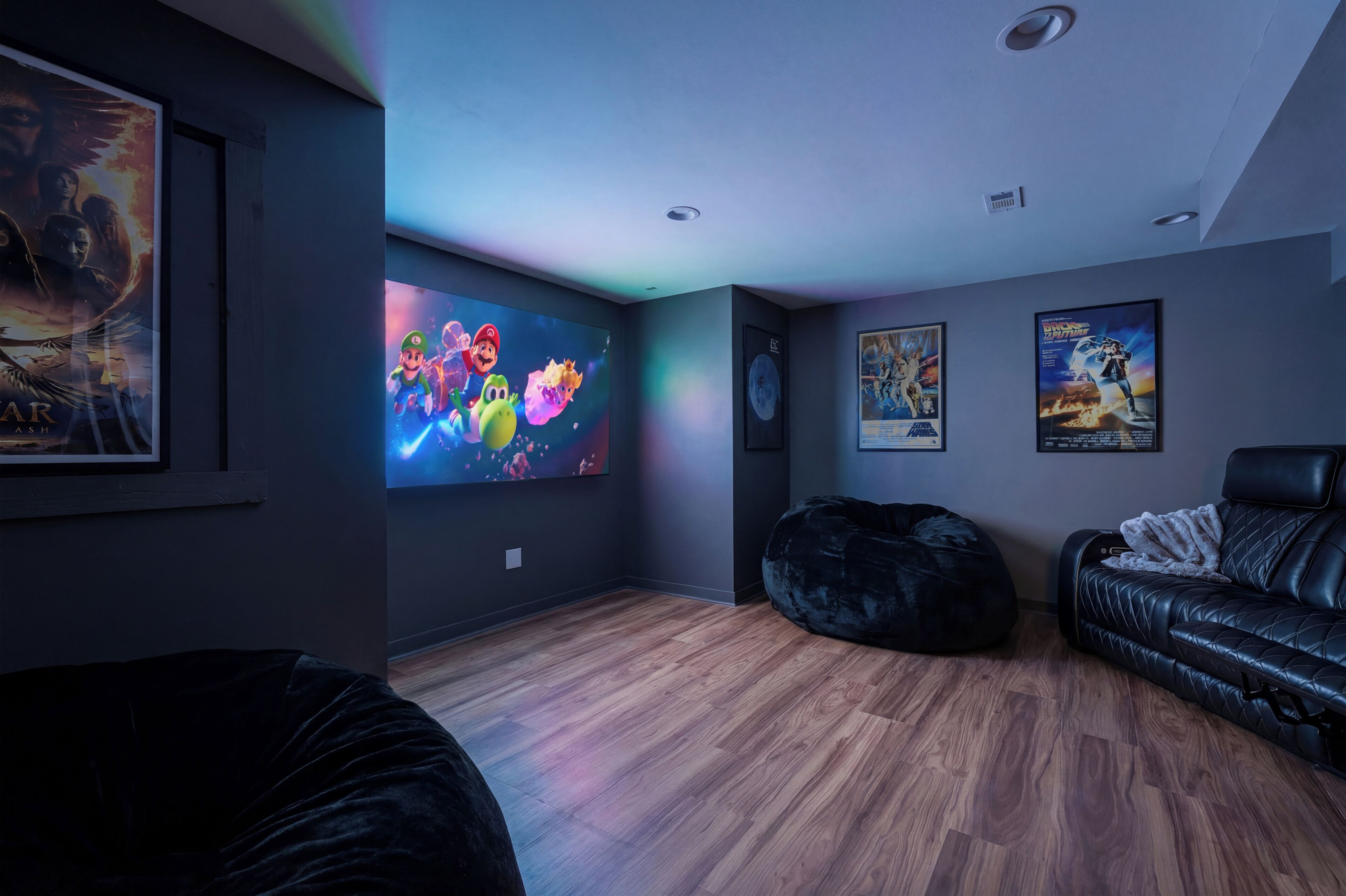 A modern living room with a flat-screen TV, a black leather couch, a black bean bag, and a wooden floor.