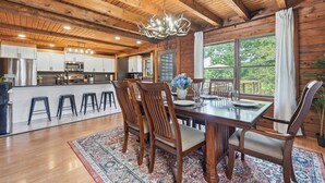Een houten chalet van binnen met een eethoek, keuken en grote ramen.