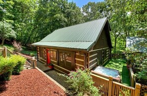Eine Blockhütte mit Metallbedachung, umgeben von einer Holzterrasse und einem Whirlpool.