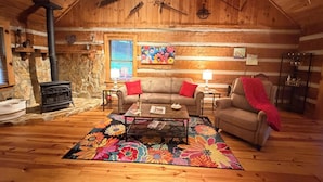 A cozy cabin interior with a fireplace, wooden walls, a sofa, a coffee table, and a colorful rug. - Storybook Cabin-Hot Tub, Fire Pit & Tree Top Views (Ellijay)