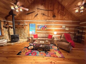Ein gemütliches Blockhäuschen mit Kamin, Holzwänden, einer Couch, einem Couchtisch und einem farbenfrohen Teppich.