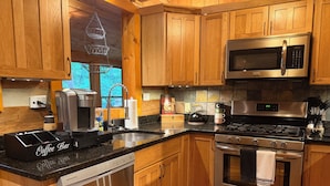 A kitchen with wooden cabinets, stainless steel appliances, a coffee bar, and a colorful rug. - Storybook Cabin-Hot Tub, Fire Pit & Tree Top Views (Ellijay)