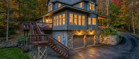 A two-story house with a stone foundation, a wooden deck, and a garage.
