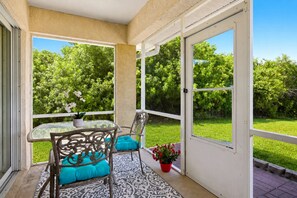 Eine überdachte Terrasse mit Tisch und Stühlen, einem Blumentopf und Blick auf eine grüne Landschaft.