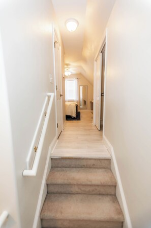 A carpeted staircase leading to a bedroom with a bed, a window, and a ceiling light. - 4bdrm/Gym/Arcade/Theater/Jacuzzi (New Bern)