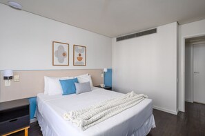 A hotel room with a bed, bedside table, lamp, wall art, and a door. - Suite na Berrini by Conviva (São Paulo)