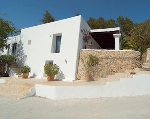 Un bâtiment blanc avec un mur en pierre, des plantes en pot et un escalier menant à une entrée abritée.