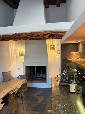 Een gezellig interieur met een open haard, houten balken in het plafond en hangende lampen.