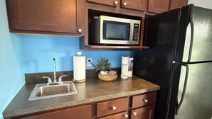 A kitchen with wooden cabinets, a stainless steel sink, a microwave, a refrigerator, and a countertop with a plant and a coffee maker. - Aeries Villas 309 A (Grafton)