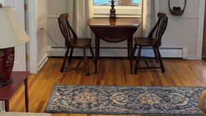 Un comedor con una mesa, dos sillas, una lámpara, un tapete y una ventana con cortinas.