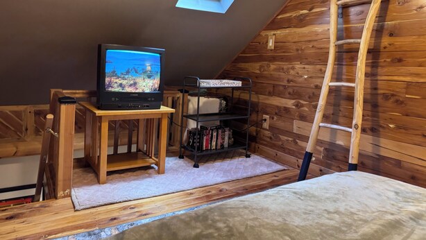 Dormitorio tipo loft con televisor, estanterías de madera, una escalera y un tragaluz.
