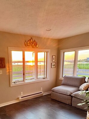 A room with a large window, a gray sofa, and a view of a landscape.