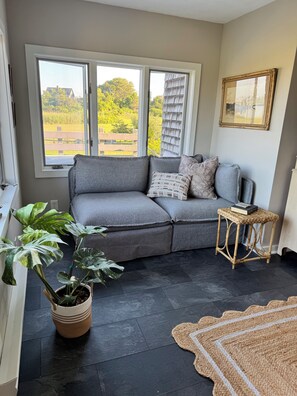 Una habitación con un sofá gris, una mesita de mimbre, una planta en maceta y una alfombra.