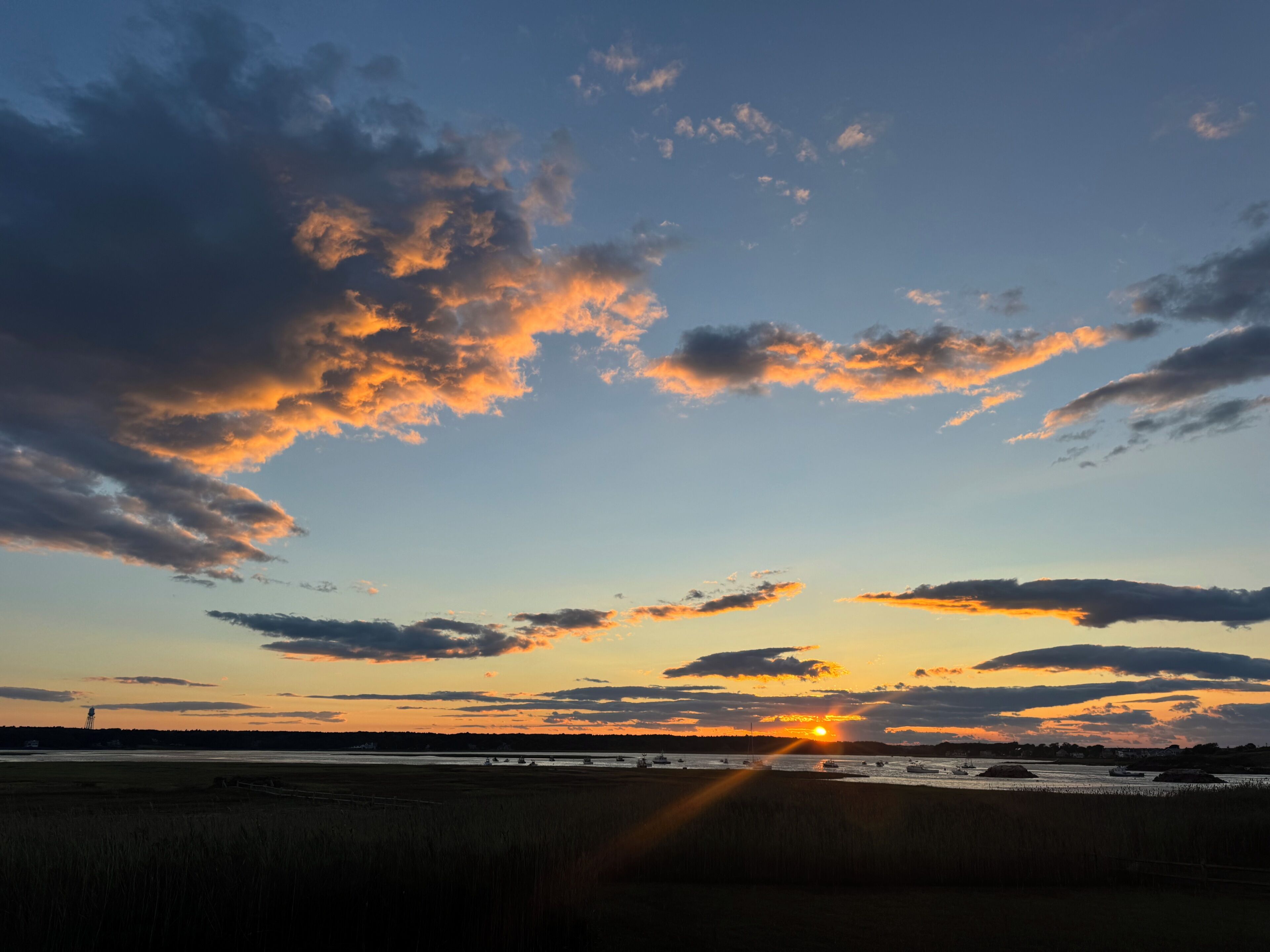 Solnedgang over et fladt landskab med både på vandet og en klar himmel.