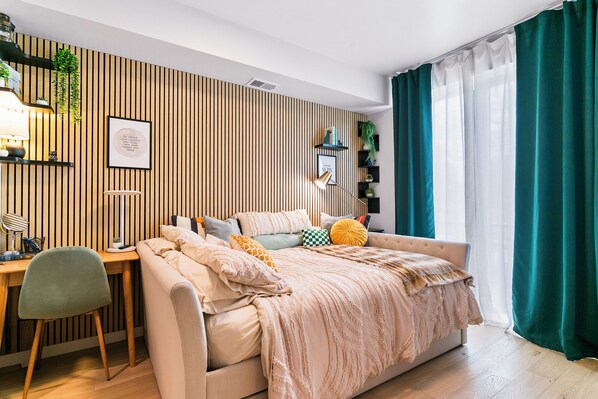 A modern bedroom with a bed, a desk, and a chair. There is a wall with vertical wooden slats and a window with curtains.
