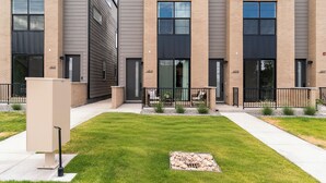 A modern multi-story building with numbered doors, a well-maintained lawn, and a small garden area. - Cozy Modern Studio - near Train, Lake & Stadium (Denver)