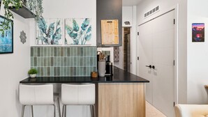 Une cuisine moderne avec un plan de travail noir, des tabourets de bar blancs, un meuble en bois et un crédence carrelée.