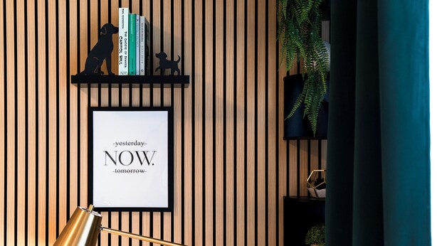 Une citation inspirante encadrée sur un mur en bois, une lampe de bureau dorée et une étagère avec des livres et des objets décoratifs.