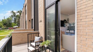 Un appartement moderne doté d’un balcon, d’un canapé, d’une petite table et d’une porte-fenêtre coulissante donnant sur un coin cuisine.