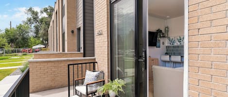 A modern apartment with a balcony, a sofa, a small table, and a sliding glass door leading to a kitchen area.