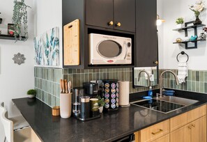 A modern kitchen with a black countertop, a coffee machine, a microwave, and a sink.