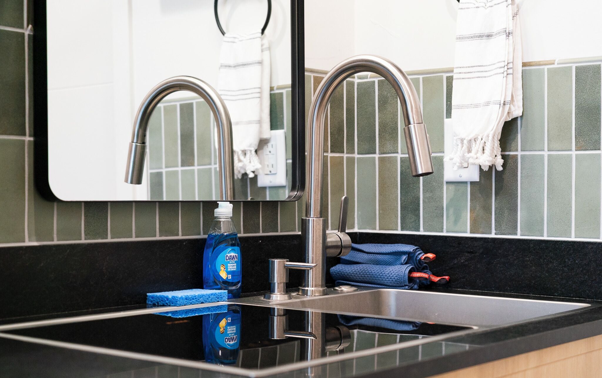 A modern bathroom with a stainless steel sink, a mirror, and a towel rack.