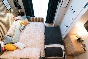 Een knus hotelkamer met een bed, nachtkastje en een klein raam.