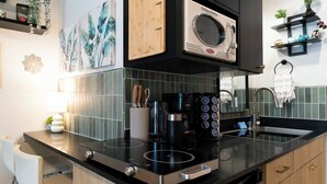 Une cuisine moderne avec un plan de travail noir, des appareils en acier inoxydable et un four à micro-ondes placé au-dessus d’un pare-feu carrelé.