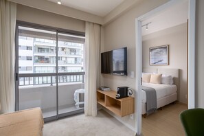 A modern hotel room with a large sliding glass door to a balcony, a bed with a headboard, a mounted TV, a small wooden shelf, and a framed picture on the wall. - Nex One Vila Nova (São Paulo)