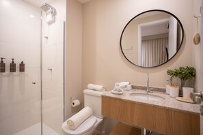 A modern bathroom with a glass shower enclosure, a toilet, a sink with a mirror, and toiletries. - Nex One Vila Nova (São Paulo)