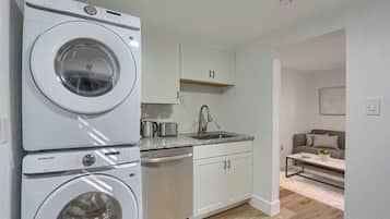 A compact kitchen with a washing machine, a sink, cabinets, and a small seating area.