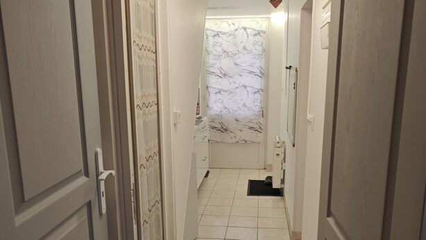 Un pasillo estrecho con suelo de baldosas blancas, una puerta a la izquierda y otra a la derecha.